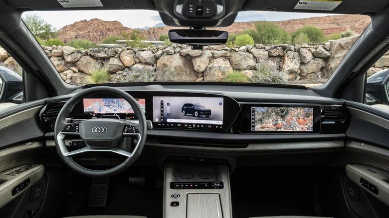 Wide shot of the dashboard in the Q9 showing its three screens and a rock wall with shrubs growing and some mountains visible out the windshield