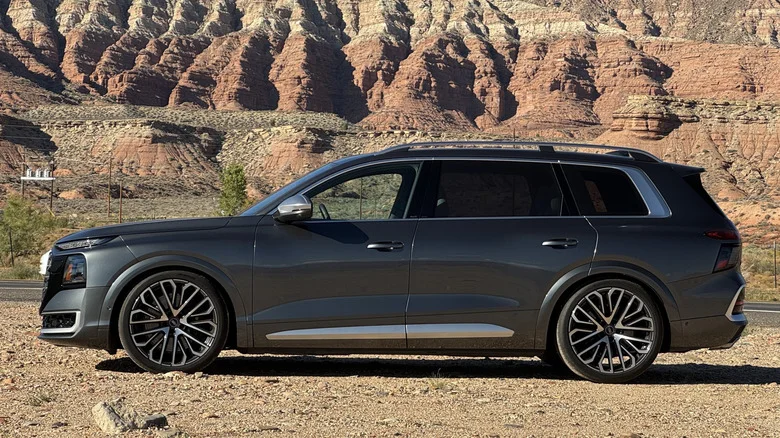 Side view of the dark gray SQ9 parked on dirt in front of a view of red and brown mountains