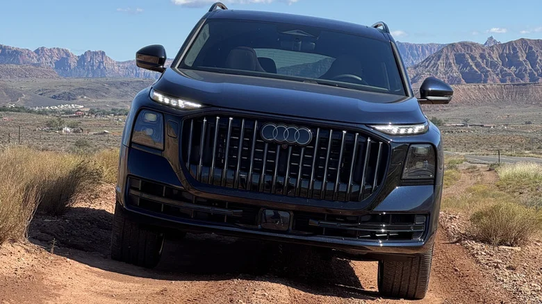 Head-on shot of the dark blue Q9 parked on a shrubby dirt trail in front of a blue sky and a mountain range