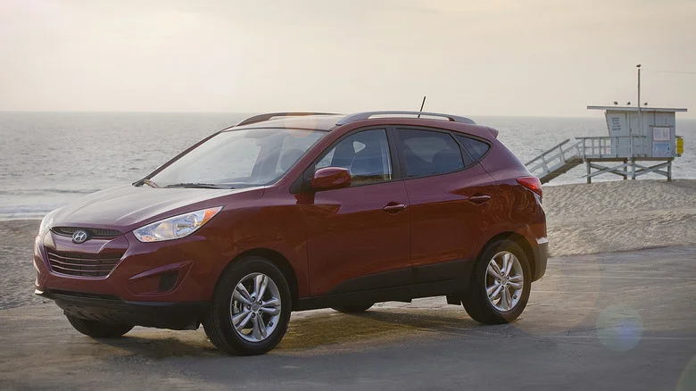A red 2010 Hyundai Tucson in front of a beach with a lifeguard stand in the background.