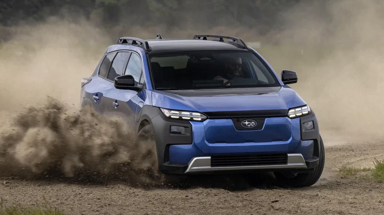 A blue Subaru Trailseeker speeding around a corner on a gravel road, kicking up stones and dust.